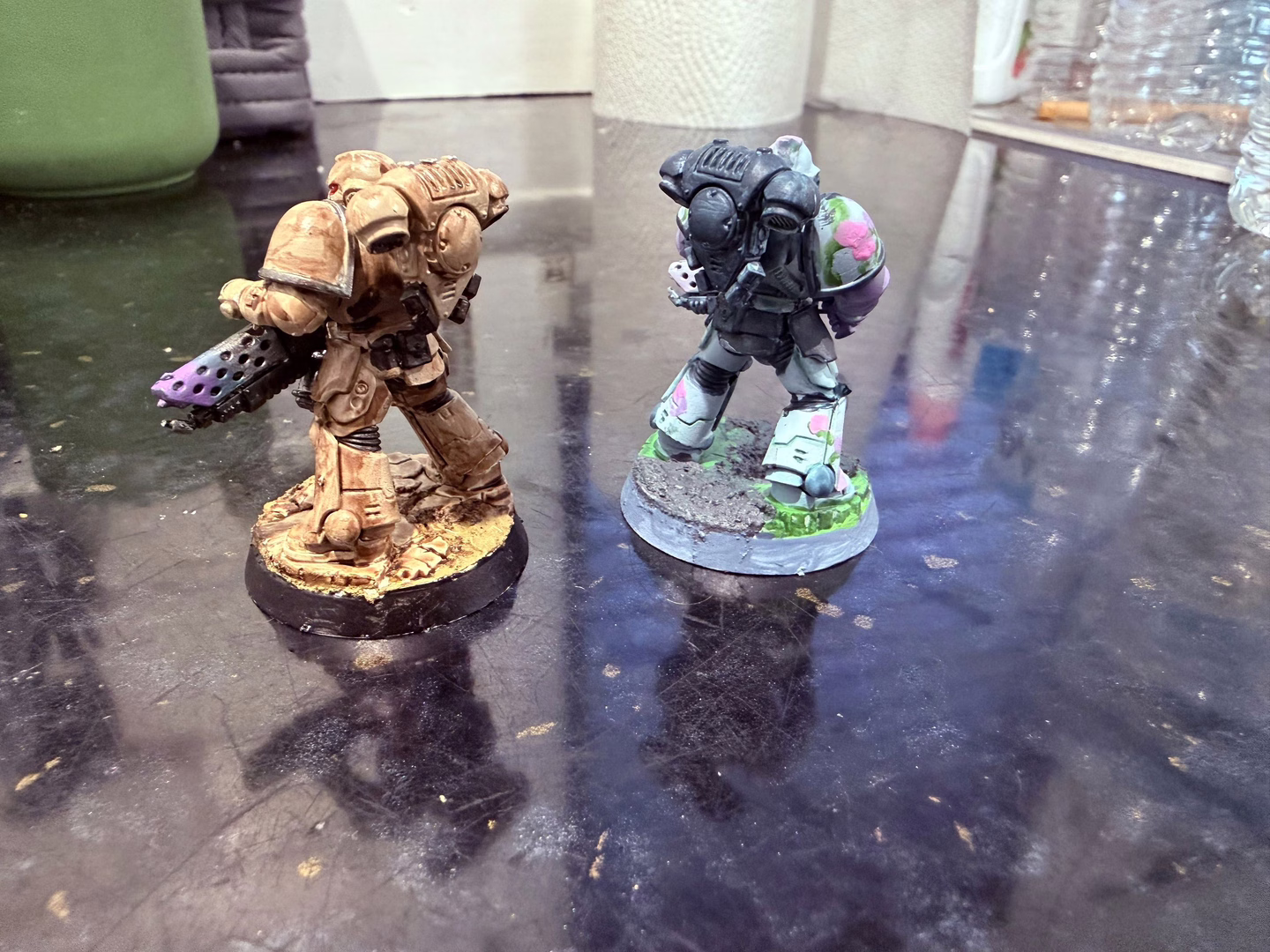 Rear view of 2 painted Space Marine miniatures, one in tan and one with a flowery baby blue pattern